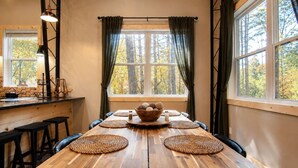 Une table à manger en bois, agrémentée de sets de table en fibres tressées, un bol de noix et une fenêtre avec des rideaux.