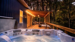 Un bain à remous situé dans un espace boisé, avec une terrasse en bois et un coin salon abrité.