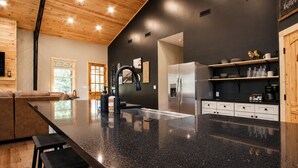 Une cuisine moderne dotée d’un grand îlot central, d’appareils électroménagers en acier inoxydable et d’un plafond en bois.