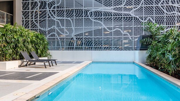 A swimming pool with a modern architectural backdrop, surrounded by greenery and lounge chairs.