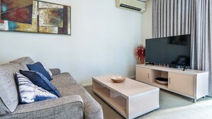 A modern living room with a grey sofa, a coffee table, a flat-screen TV on a wooden stand, and a large abstract painting on the wall.
