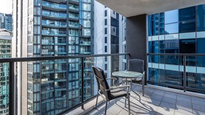 A balcony with a chair and table, large windows, and a view of high-rise buildings.