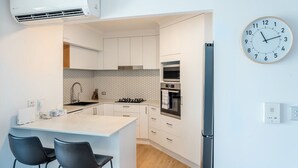 Une cuisine moderne avec des meubles blancs, un îlot central doté de chaises, un four encastré et une horloge murale.
