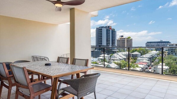 A balcony with a dining table, chairs, and a ceiling fan.