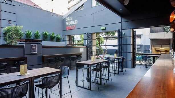 Un espace extérieur aménagé avec des tables et des chaises, un bar et une enseigne indiquant « Old World Bistro ».