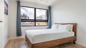 Une chambre d’hôtel moderne avec un lit en bois, une grande fenêtre avec des rideaux et une vue sur les bâtiments de la ville.
