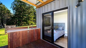 A modern outdoor kitchen with a wooden countertop and a sink, adjacent to a bedroom with a bed and a nightstand.