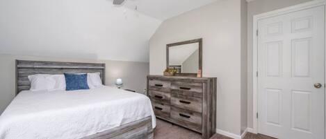 Une chambre à coucher avec un lit, une commode, un ventilateur de plafond et une porte.