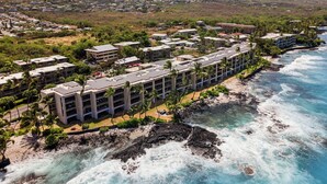 Vista aérea de un hotel costero con varias edificaciones, una playa y un litoral rocoso.