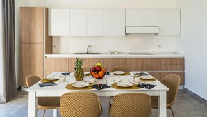 A modern kitchen with white cabinets, a dining table set for four with wicker chairs, and a fruit bowl on the table.