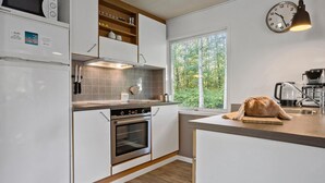 A modern kitchen with white cabinets, a built-in oven, a microwave, and a window with a view of trees. - 3 bedroom pet friendly home in Toftlund (Toftlund)