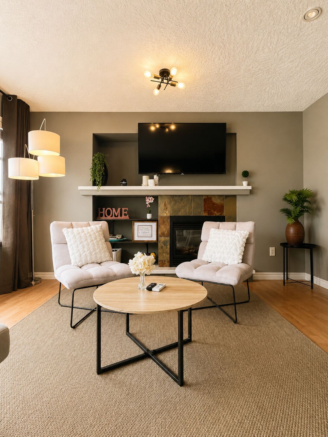 A living room with two sofas, a coffee table, a TV mounted above a fireplace, and a ceiling light fixture.