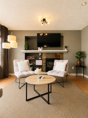 A living room with two sofas, a coffee table, a TV mounted above a fireplace, and a ceiling light fixture.