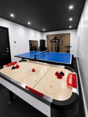 A ping pong table with surrounding exercise equipment, a door, and a wall-mounted bike.
