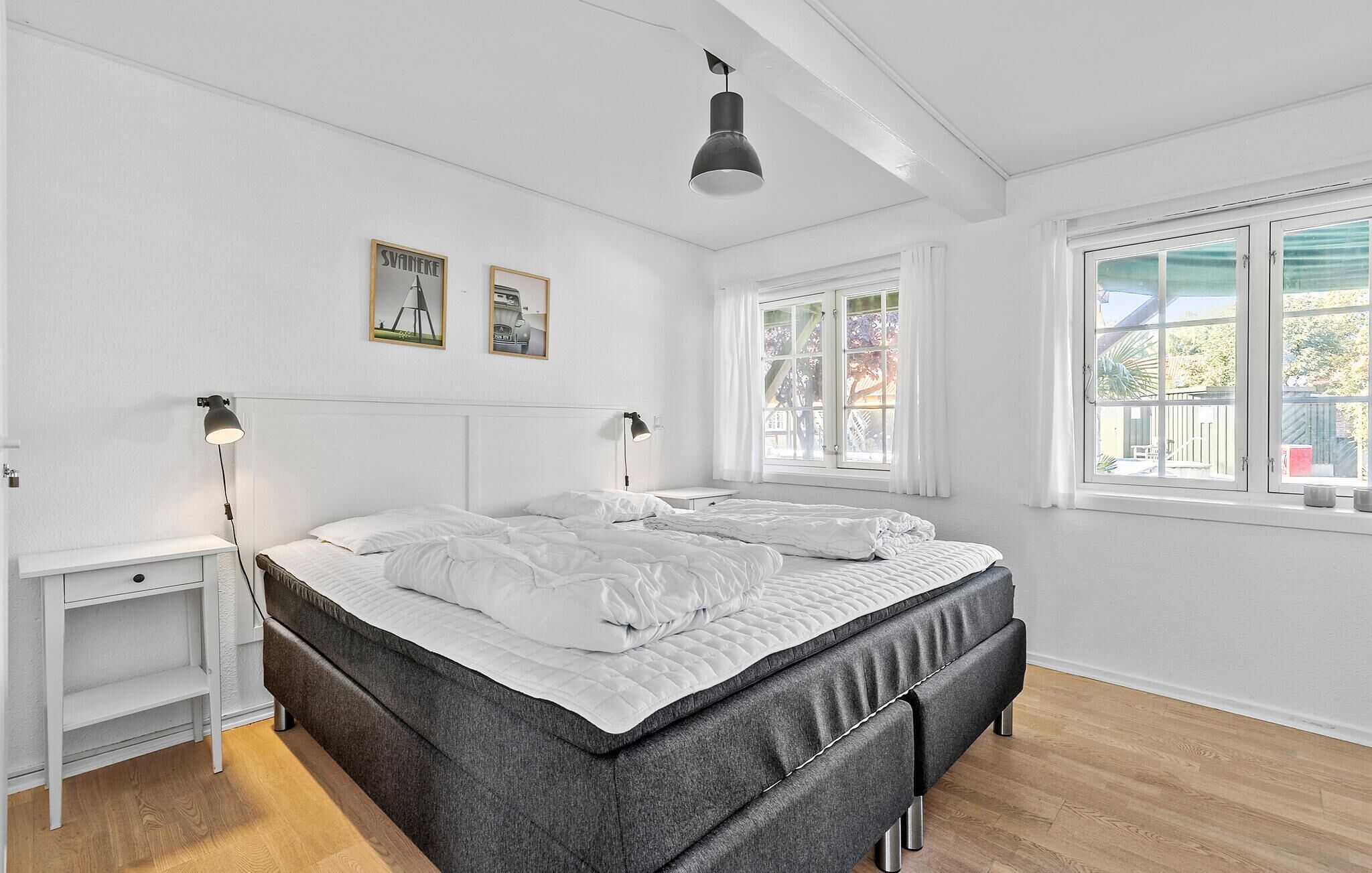 Quarto com uma cama grande, duas mesas de cabeceira, um candeeiro pendente e uma janela com cortinas.