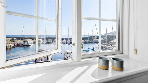 A bay view through a large window with two ceramic mugs on the sill. - Beautiful apartment in Svaneke with swimming pool (Svaneke)