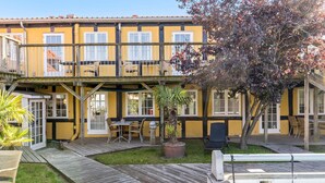A yellow building with a wooden deck, a pool, and outdoor seating. - Beautiful apartment in Svaneke with swimming pool (Svaneke)