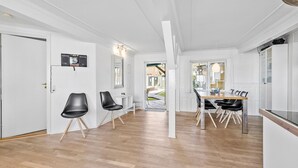 A modern kitchen with a wooden table and black chairs, white walls, and a view of the backyard. - Beautiful apartment in Svaneke with swimming pool (Svaneke)