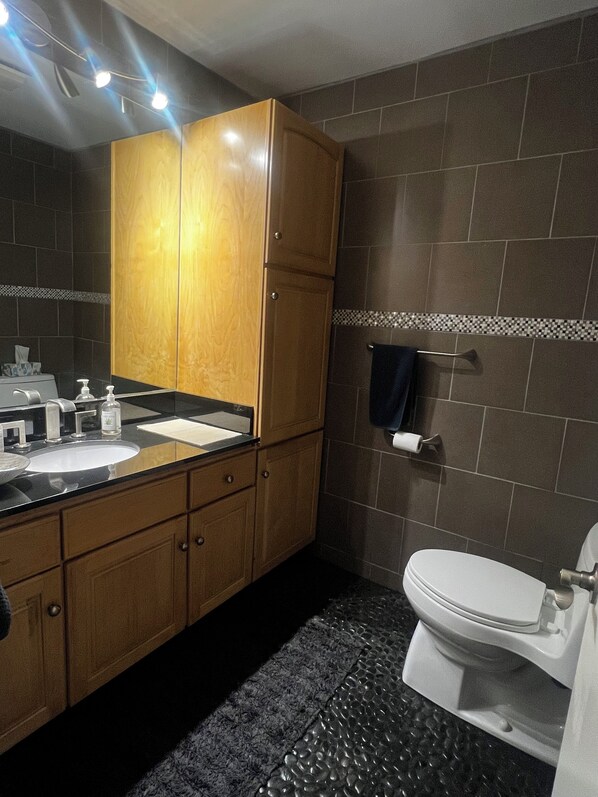 Un baño con tocador de madera, un lavamanos, un espejo, un perchero para toallas y un inodoro.