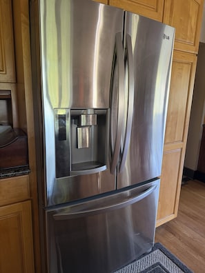 Ein eingebauter, edelstahlfarbener Kühlschrank mit Wasserspender in einer Küche mit Holdekor-Schränken und einer Arbeitsplatte aus Granit.