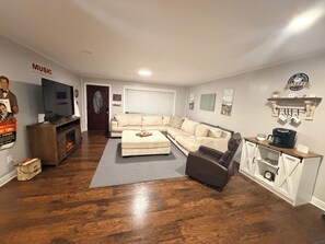 Een woonkamer met een hoekbank, een televisie, een koffiehoek en een muur met een bord van een koffietent.