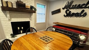 A dining area with a round wooden table, black chairs, a brick fireplace, and a vintage car display. - 3-bedroom w/pool and all the comforts of home in Muscle Shoals-recording capital (Muscle Shoals)