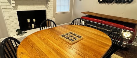 A dining area with a round wooden table, black chairs, a brick fireplace, and a vintage car display.
