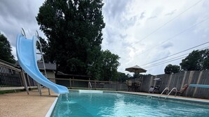 A swimming pool with a blue slide, surrounded by a pebble deck. - 3-bedroom w/pool and all the comforts of home in Muscle Shoals-recording capital (Muscle Shoals)