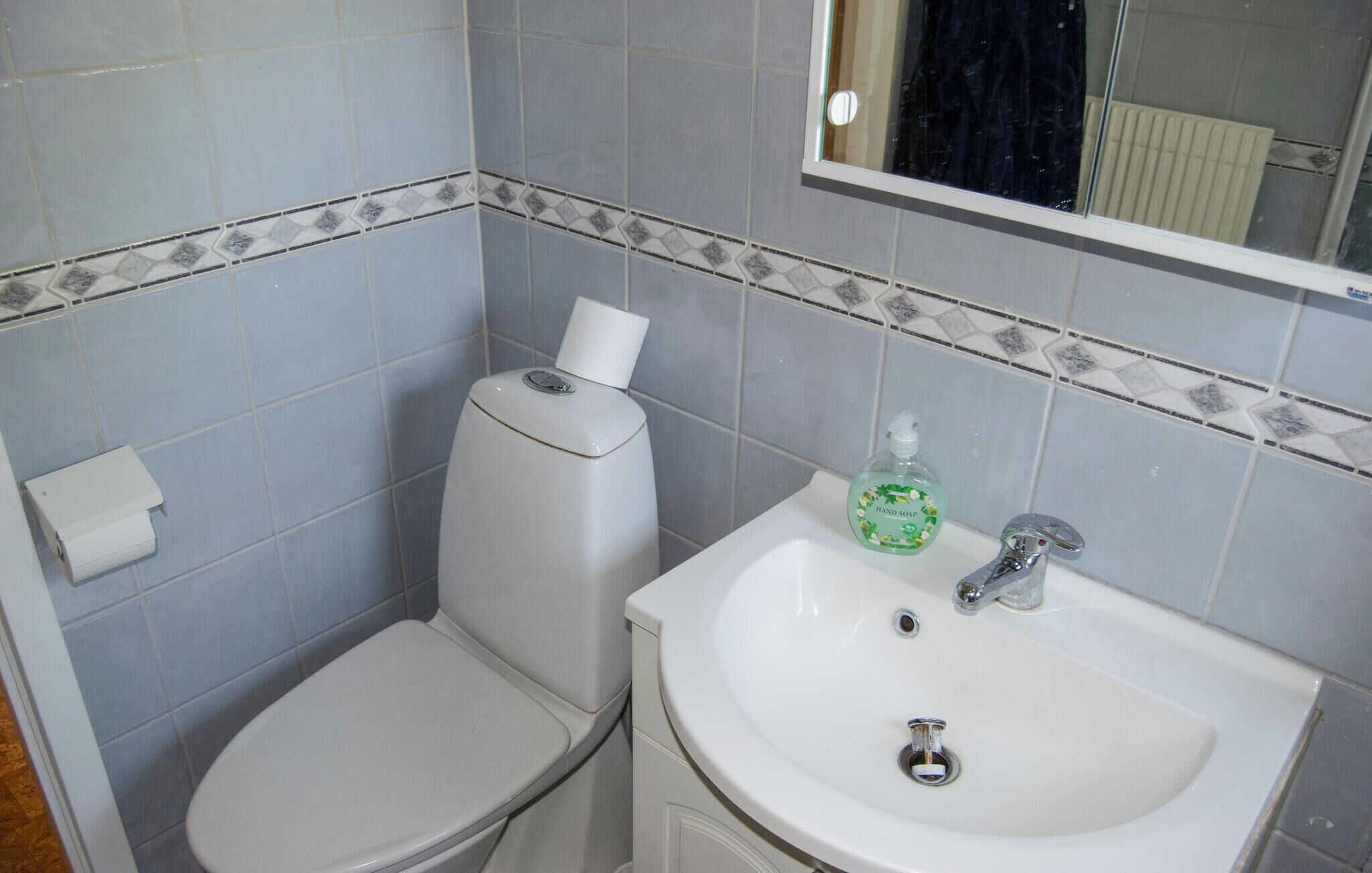 A bathroom with a toilet and sink, tiled walls, and a window.