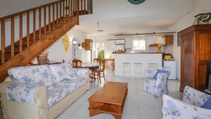 A spacious living room with a wooden staircase, a dining area, and a kitchen with a bar. - 3 bedroom gorgeous home in Cervione (Cervione)