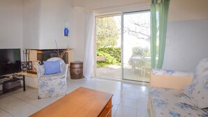 A living room with a sofa, a wooden table, a television, and a window with a view of a garden. - 3 bedroom gorgeous home in Cervione (Cervione)