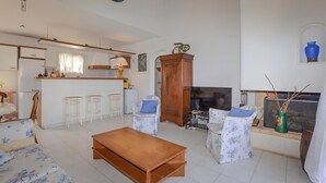 A living room with a wooden coffee table, two patterned armchairs, a TV, and a kitchen area with a bar counter and stools. - 3 bedroom gorgeous home in Cervione (Cervione)