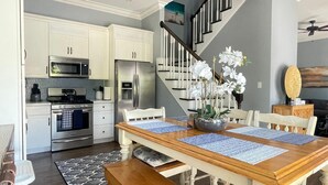 A modern kitchen with white cabinets, stainless steel appliances, and a wooden dining table with blue placemats.