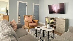 A living room with a sofa, armchair, coffee table, and a flat-screen TV mounted on the wall.