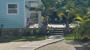 A light blue building with a sloped roof, a stone pathway leading to the entrance, and a small garden with palm trees.