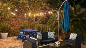 An outdoor patio with wicker furniture, a blue table, and string lights.