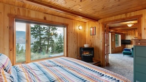 A cozy cabin room with a large bed, a fireplace, and a view of the outdoors. - Stunning Mountain & Lake Views 3BR Cabin with Hot tub (Twin Lakes)
