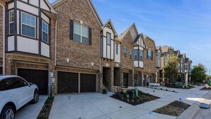 A row of townhouses with attached garages, a paved driveway, and a landscaped front yard. - Stylish Arcade Stay EV Central (Lewisville)