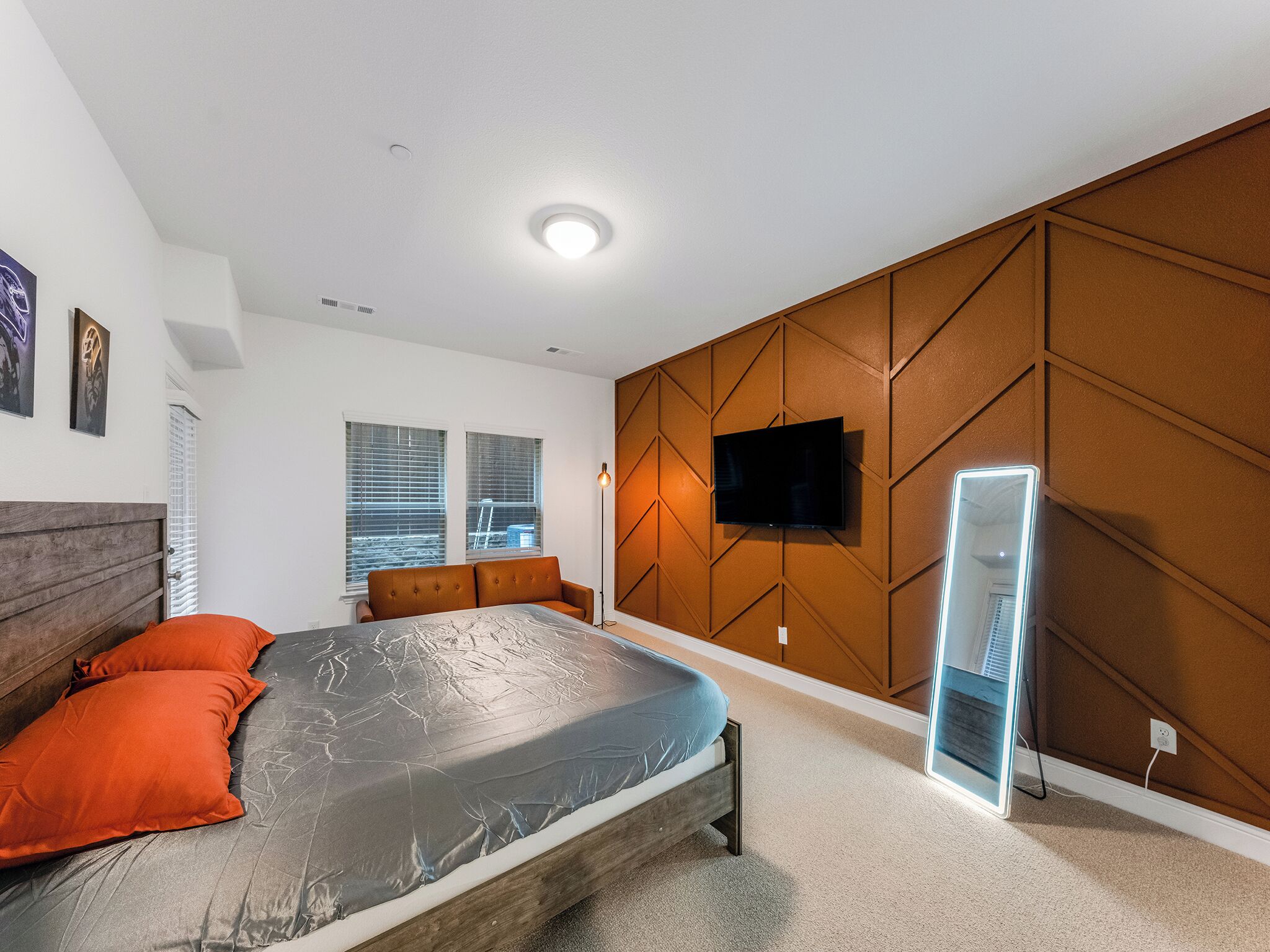 A modern bedroom with a bed, a TV mounted on a wooden panel wall, and a large mirror.