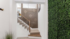 A staircase with a geometric patterned wall, a wooden handrail, and a green wall covered in foliage at the bottom. - Stylish Arcade Stay EV Central (Lewisville)