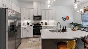A modern kitchen with white cabinets, stainless steel appliances, and a central island with bar stools. - Stylish Arcade Stay EV Central (Lewisville)