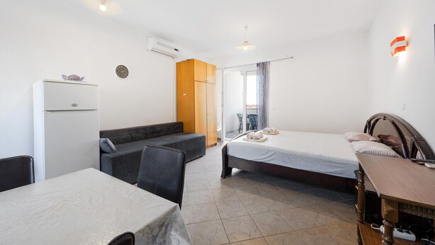 Une chambre d’hôtel comprenant un lit, un canapé, une table, un appareil de climatisation, une horloge et une porte coulissante donnant sur un balcon.