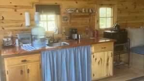 A wooden cabin kitchen with a large island, a water dispenser, a coffee maker, and a kettle. - The Superior Bunkhouse, a Cozy 16 X 24 Cabin near Grand Marais MN and Hovland MN (Hovland)