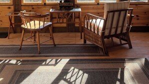 A wooden cabin interior with a large window, a clock, a welcome sign, and a dining area with chairs and a table. - The Superior Bunkhouse, a Cozy 16 X 24 Cabin near Grand Marais MN and Hovland MN (Hovland)