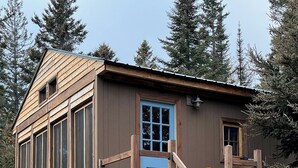 A wooden cabin with a blue door, wooden railings, and a staircase leading to a deck. - The Superior Bunkhouse, a Cozy 16 X 24 Cabin near Grand Marais MN and Hovland MN (Hovland)