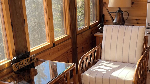 A cozy cabin interior with wooden walls, a glass table, a cushioned chair, and a 'WELCOME' sign. - The Superior Bunkhouse, a Cozy 16 X 24 Cabin near Grand Marais MN and Hovland MN (Hovland)