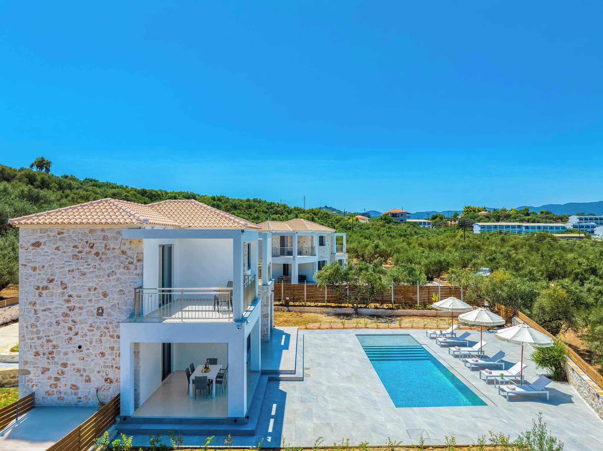 A modern villa with a stone facade, a swimming pool, and a view of the surrounding landscape.