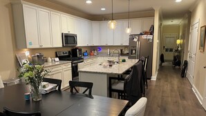 Een moderne keuken met witte kasten, een centraal eiland en een eethoek met een donker houten tafel en stoelen.