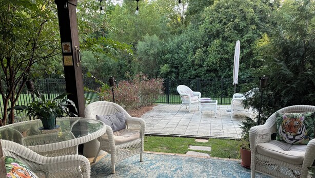 Een terras met rieten meubels, een glazen tafel en een kamerkleed met dessin.