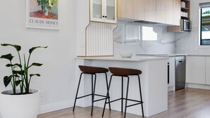 Eine moderne Küche mit weißen Schränken, einer Marmor-Spritzschutzleiste und einer zentralen Kochinsel mit Barhocker.